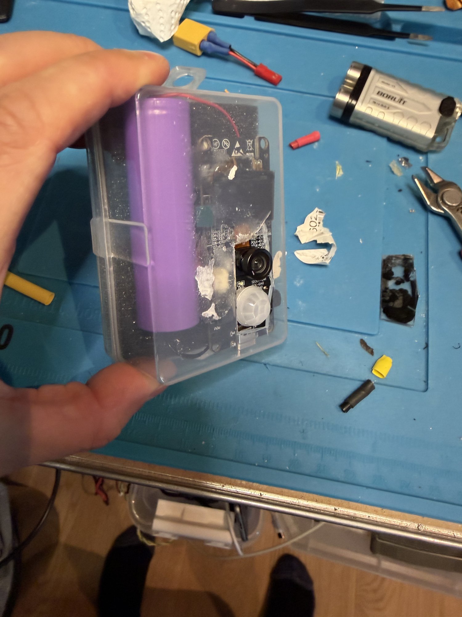 Holding the plastic box with the camera and PIR dome visible through the lid