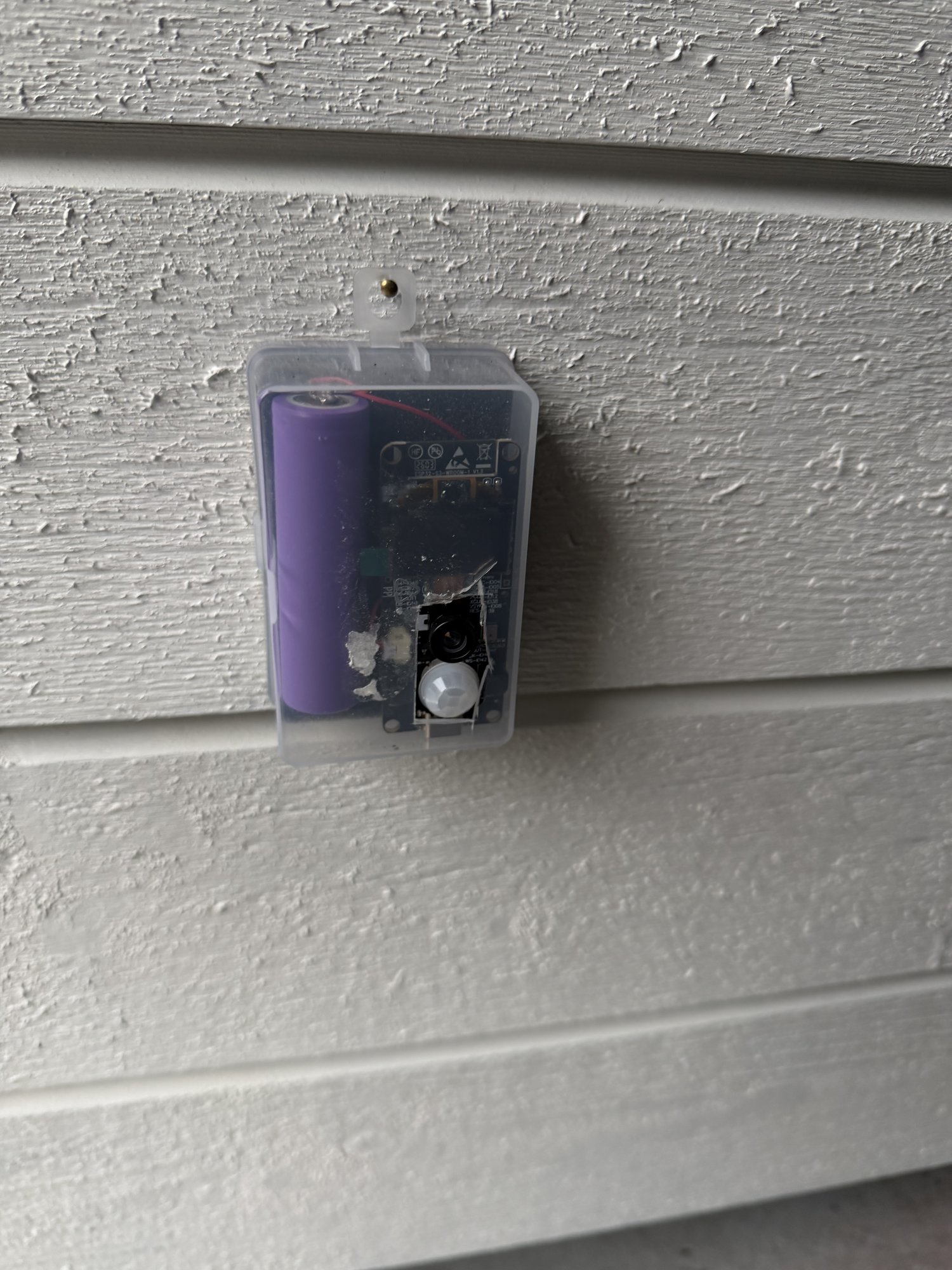 The plastic box camera mounted on the white wooden wall outside